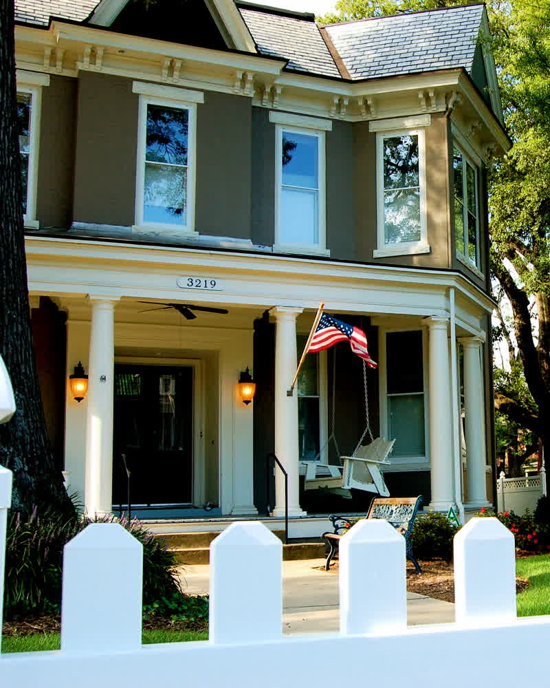 A painted Victorian house with a deep columned porch and white picket fence under shade trees on Grove Avenue